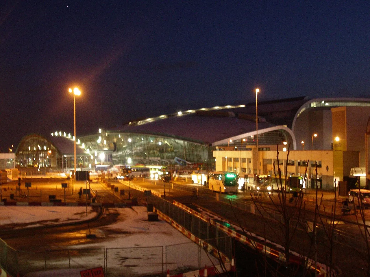 Terminal 2 van Dublin Airport, verlicht in de avond, met bussen en verkeer ervoor